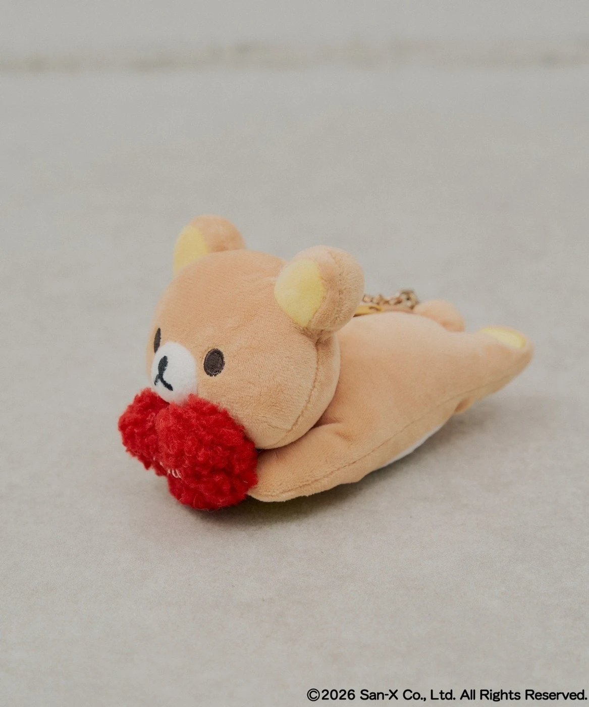 赤いハートを抱えたリラックマのぬいぐるみチャーム。公式カラーはブラウンで、トートとは別売